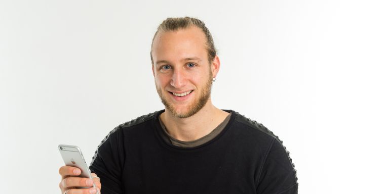 Junger Mann lächelt und hält sein Handy in der Hand