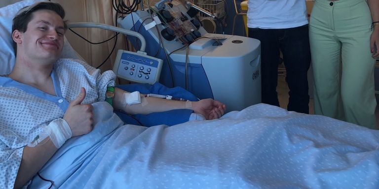 Männlicher Spender liegt während Spende im Spitalbett und reckt Daumen in die Höhe