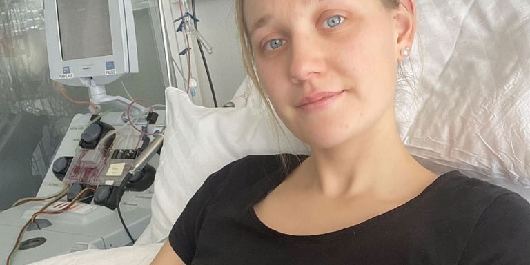 Marion, ene junge Frau mit blondem Haar und blauen Augen, liegt in einem Spitalbett und spendet ihre Blutstammzelle. Im Hintergrund ist das Apharesegerät zu sehen.