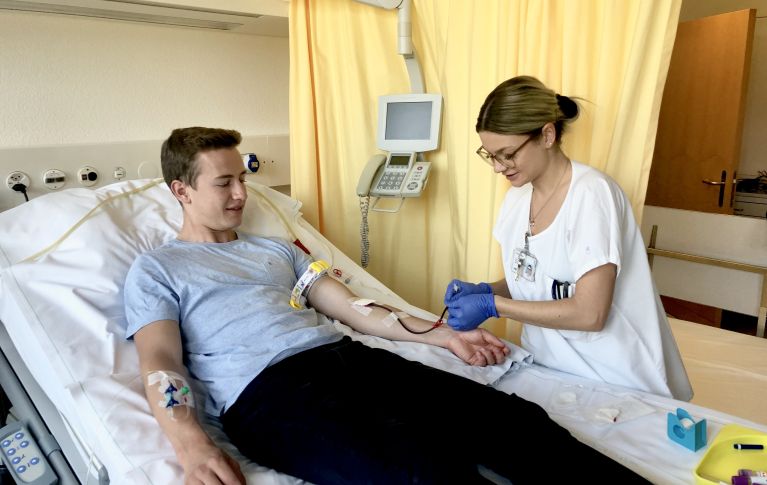La photo montre un jeune homme et une infirmière préparant l'accès veineux pour le don de cellules souches du sang périphérique.