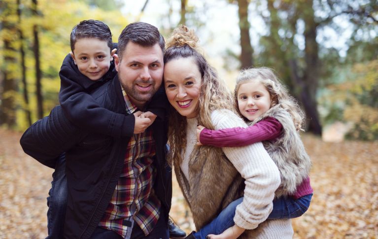 La photo montre un homme et une femme avec leurs deux enfants. Tous sourient à la caméra, heureux.