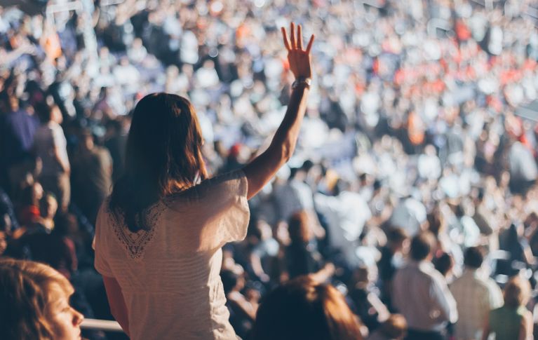 Una sala piena di gente, una donna alza la mano