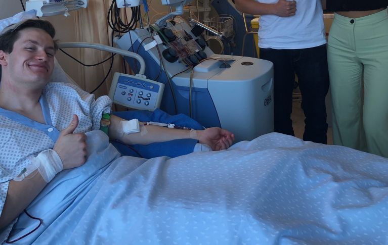 Männlicher Spender liegt während Spende im Spitalbett und reckt Daumen in die Höhe