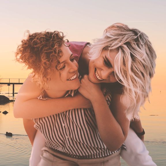 Zwei junge Frauen nehmen sich Huckepack am Strand