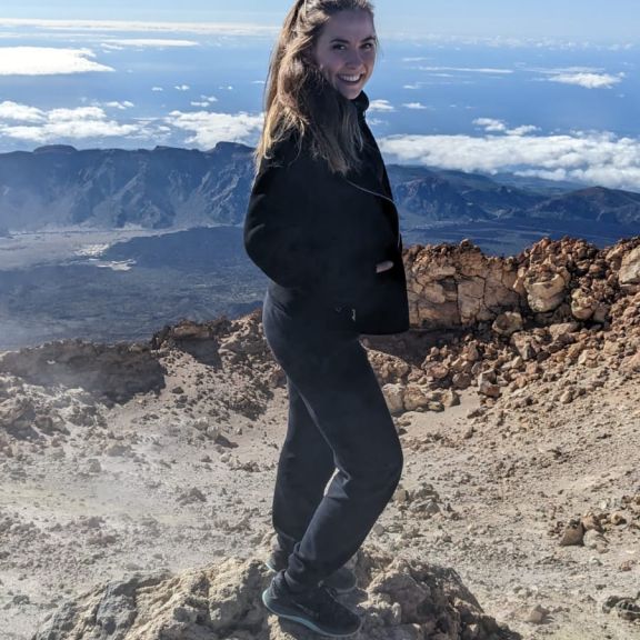 Ladina Gall en randonnée sur un sentier pierreux, à l’arrière-plan une vaste vue sur la vallée avec quelques nuages.