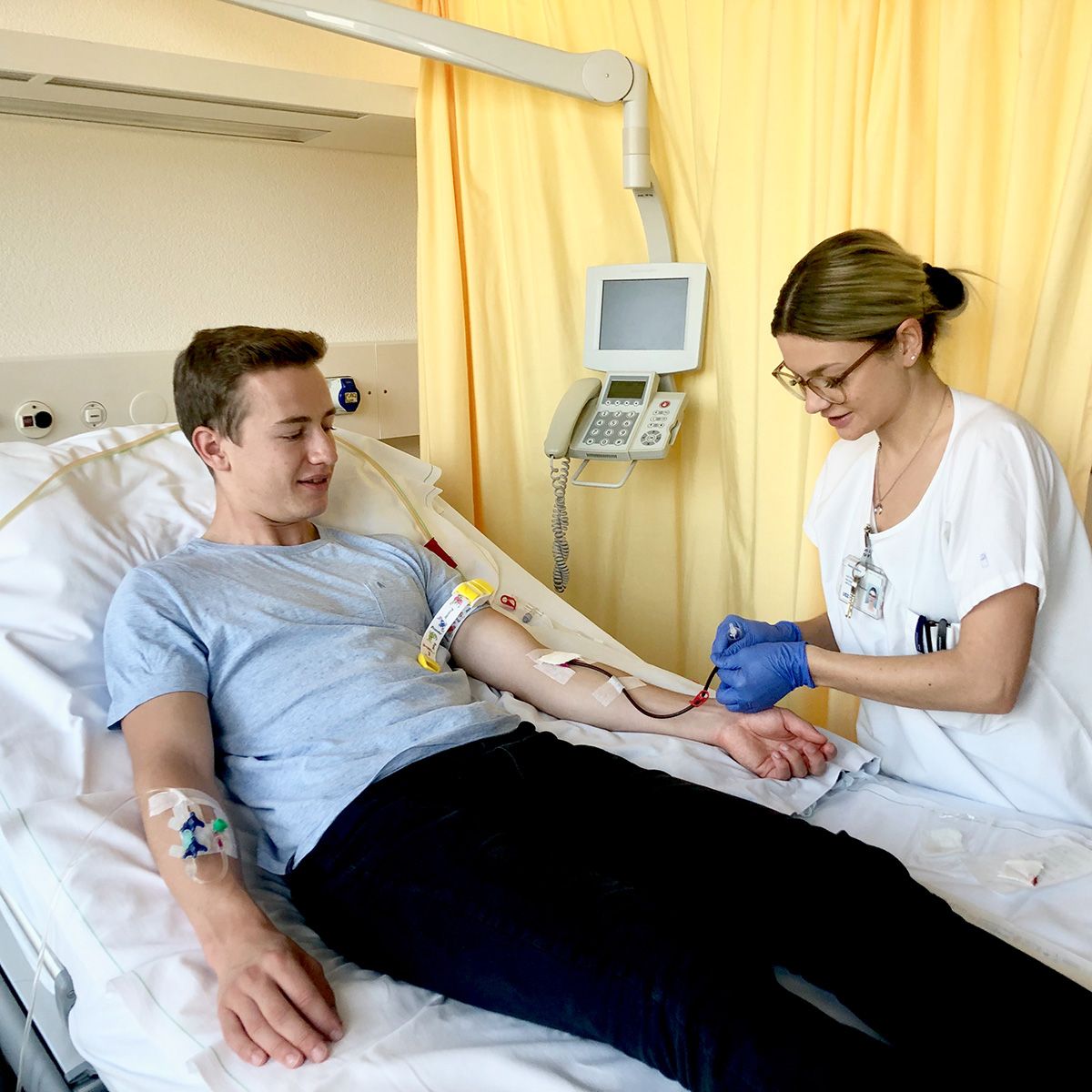 Ein junger Mann liegt in einem Krankenhausbett und wird auf die periphere Blutstammzellspende vorbereitet.